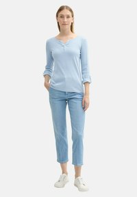 Camisa de manga larga azul clara con cuello redondo y acentos de botones, combinada con jeans recortados azul claros y zapatillas blancas.