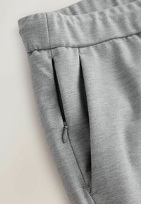 Gray athletic pants with a smooth texture, featuring a zippered side pocket and pleated detailing at the waistband.