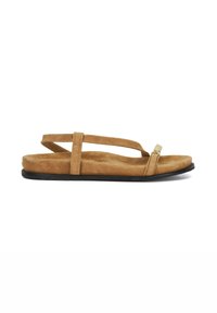 Tan suede sandal with a flat black sole, featuring two crisscrossing straps and a decorative metallic accent on the toe.