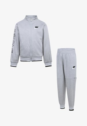 Ensemble de survêtement Nike gris comprenant une veste zippée avec le texte "JUST DO IT" et un pantalon ajusté assorti avec taille élastique et poche latérale.
