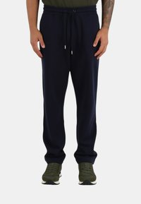 Pantaloni della tuta blu navy con vita elastica e coulisse regolabile. Vestibilità ampia, realizzati in tessuto morbido. Abbinati a scarpe sportive verdi.