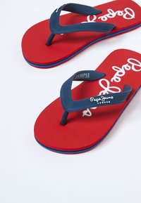 Czerwone klapki ze granatowymi paskami z logo "Pepe Jeans London" na białym tle.