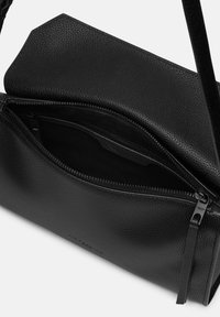Borsa a tracolla in pelle nera con finitura testurizzata, dotata di chiusura con zip e tasca interna. Gli accenti includono un logo sottile all'esterno.