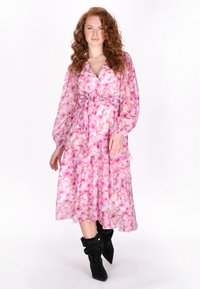 Bloemen wikkeljurk met een roze en witte print, lange doorzichtige mouwen, een strakke tailleband en een gelaagde rok, gecombineerd met zwarte enkellaarzen.