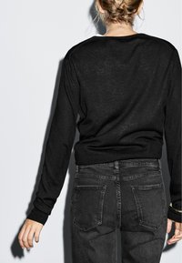 Maglione nero a maglia con maniche lunghe, polsini a costine e una vestibilità comoda, abbinato a jeans grigio scuro con tasche posteriori e una leggera scoloritura.