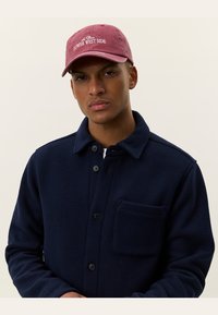 Navy fleece shirt jacket with a button front and chest pocket. Burgundy baseball cap featuring "Lower West Side" embroidered in white.