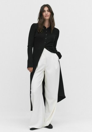 Black ribbed cardigan with button closure, long sleeves, and slit sides, paired with white wide-leg trousers made of soft fabric.