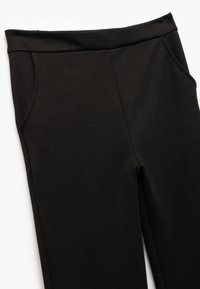 Svarta tight byxor med resårmidja och sidofickor på vit bakgrund.