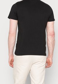 Camiseta negra de manga corta hecha de algodón, con escote redondo y corte recto. Textura suave con detalles de costura sutiles.