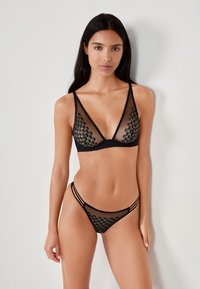 Black lingerie set featuring a sheer bra with round accents and a matching sheer thong with triple side straps, highlighting a geometric design.