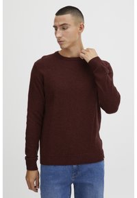 Maroon knitted sweater with a crew neck and ribbed cuffs. The fabric appears soft with a slight texture. Paired with blue jeans.