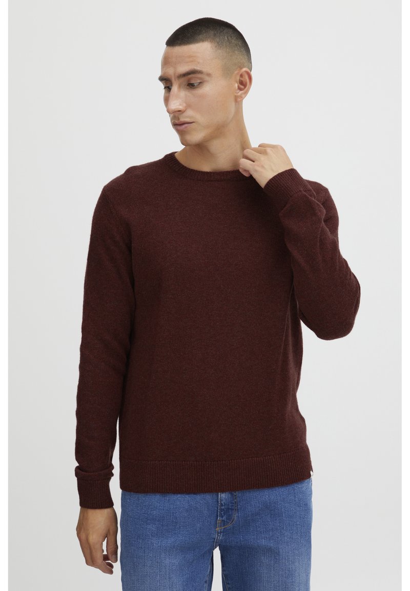 Maroon knitted sweater with a crew neck and ribbed cuffs. The fabric appears soft with a slight texture. Paired with blue jeans.