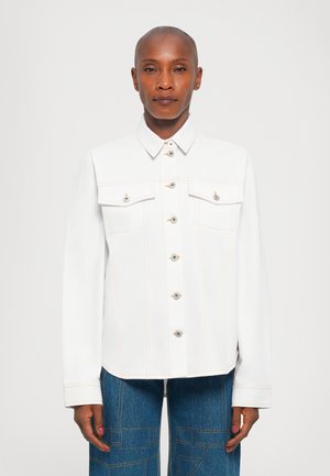 Vit denimjacka med spetsig krage, knappstängning fram, två bröstfickor och kontrasterande orange sömmar. Slät, strukturerad passform.