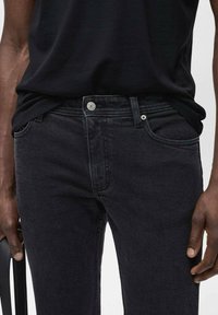 Vaqueros de mezclilla negros con un corte ajustado, que presentan un diseño clásico de cinco bolsillos, cierre de botón y sutiles detalles de costura.