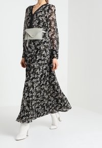 Czarna kwiecista maxi sukienka z długimi rękawami i głębokim dekoltem w kształcie litery V, w połączeniu z jasnoszarym torebką na ramię i białymi botkami za kostkę.