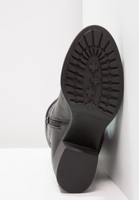 Botte en cuir noir avec une semelle texturée, un détail de fermeture éclair sur le côté et un talon effilé. Taille 37 indiquée sous la semelle.