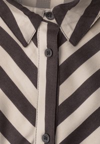 Gros plan sur un col de chemise beige rayé marron foncé boutonné avec trois boutons visibles sur le devant.