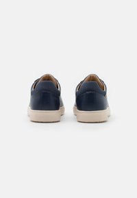 Zapatillas de piel navy con textura suave, suelas de goma blanca y diseño minimalista. Presentan bordes redondeados y un cuello acolchado.