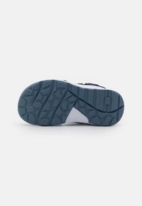 Sole di scarpa atletica blu navy e bianca con una superficie in gomma testurizzata, caratterizzata da un motivo a zig-zag geometrico per trazione e durabilità.