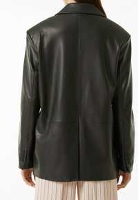 Svart läderblazer med skräddarsydd passform, breda slag och subtil lyster. Har synlig sömnad och fyra knappar som accent vid ärmarna.