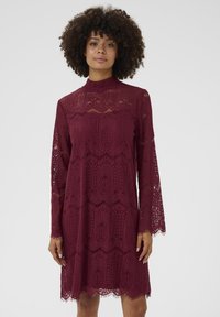 Vestido de encaje burdeos con cuello alto, mangas largas acampanadas, patrones intrincados y un dobladillo con forma de concha. Material texturizado y ligero.