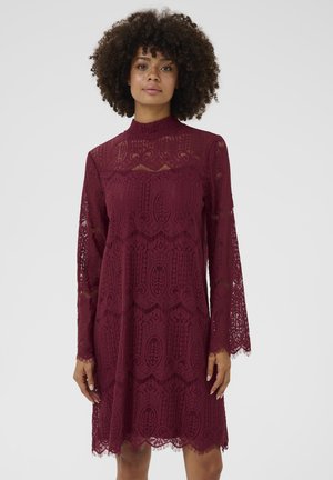 Burgundy spetsklänning med hög krage, långa trumpetärmar, intrikata mönster och en vågig nederkant. Texturerat, lätt material.