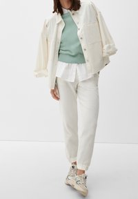 Camicia di jeans crema, maglione verde menta a trama, camicia bianca con colletto sotto, pantaloni off-white a trama e sneakers beige con dettagli neri.
