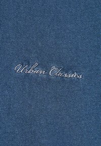 Tessuto a coste blu con una texture liscia, caratterizzato da ricami grigio chiaro della scritta "Urban Classics" in corsivo.