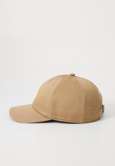 Cap in tan fabric with curved visor, embroidered yellow detail on the front, and an adjustable strap on the back. Smooth texture, classic design.