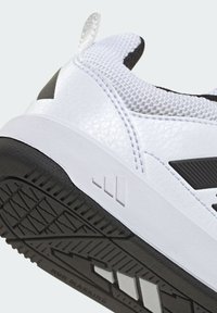 Biela športová obuv s textúrovaným zvrškom, zdobená čiernymi akcentmi a gumovou podrážkou. Súčasťou sú výrazné logo a ťahací jazýček.