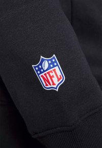 Il tessuto della felpa nera presenta un logo NFL in blu e rosso, che include un pallone da football e stelle, posizionato sulla manica.