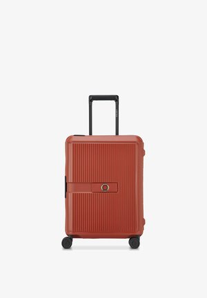 Valise rigide rouge avec des rainures verticales, poignée noire rétractable, quatre roues et fermeture à combinaison centrale sur la face avant.