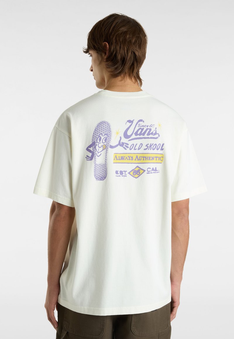 Camiseta de manga corta color crema con un estampado gráfico en la parte posterior, que presenta texto morado y una ilustración de una zapatilla, hecha de suave material de algodón.