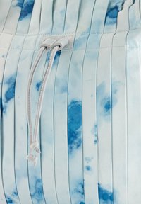 Lichtblauwe geplooide stof met donkerblauwe aquarelpatronen, voorzien van een witte trekkoord en een klein label eraan bevestigd.