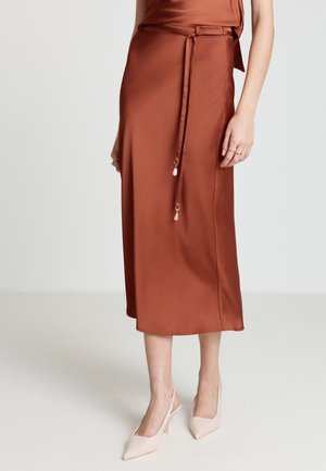 Rust-colored satin midi skirt with thin waist tie featuring two pearl charms, worn with beige pointed slingback heels.