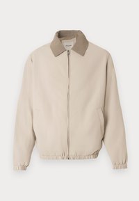 Μπεζ μπουφάν τύπου bomber με ανοιχτό καφέ γιακά, φερμουάρ μπροστά και ελαστικά μανίκια. Διαθέτει δύο πλαϊνές τσέπες και λεία, υφή υφάσματος.