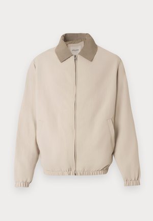 Beige bomberjakke med lysebrun krage, frontglidelås og elastiske mansjetter. Har to sidelommer og et glatt, teksturert stoff.