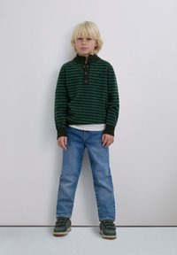 Suéter de rayas verdes y negras con cuello redondeado y tres botones, combinado con jeans azules y zapatillas verdes. Estilo sencillo y casual.