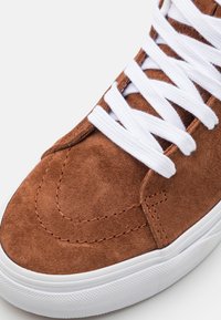 Zapatillas de ante marrón con cordones blancos, con punta redonda, detalles cosidos y suela de goma blanca texturizada.