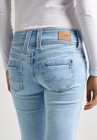 Ljust blå denimjeans med en åtsittande design, utrustade med en läderpatch vid midjan och två bakfickor med subtila sömdetaljer.