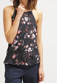 Top negro con flores que presenta un diseño de flores en rosa y blanco, tirantes de espagueti, tejido ligero y un corte holgado, combinado con pantalones azul marino.
