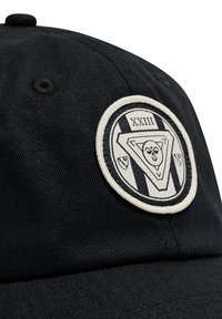 Czarna czapka materiałowa z okrągłą białą naszywką przedstawiającą rzymskie cyfry XXIII oraz geometryczny wzór twarzy w czerni i bieli.