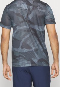 Camisa deportiva de manga corta en colores oscuros con un patrón de camuflaje. Tejido ligero y transpirable con una textura suave.