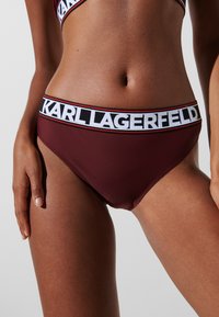 Bordo peldbikses apakšda ar melnbaltu jostas daļu, kurai ir "KARL LAGERFELD" zīmols. Gluda tekstūra, zema vidukļa dizains un minimālistisks stils.