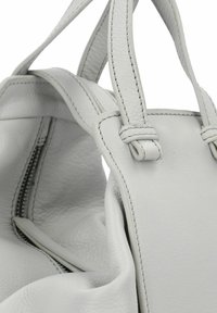 Borsa a mano in pelle bianca con doppi manici, cuciture dettagliate e tasca interna con zip visibile.