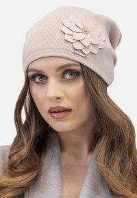 Bonnet en tricot rose clair avec une texture côtelée et une fleur en feutre décorative avec des pétales superposés et des embellissements sur le côté.