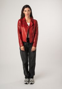 Veste de moto en cuir rouge avec des accents de fermeture éclair, portée sur une chemise blanche et assortie avec un jean noir taille haute et des baskets grises.