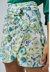 Falda con estampado floral en blanco, con diseños en azul y verde. Hecha de tela con textura, incluye detalle de nudo en la cintura.