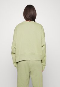 Grön bomullströja med avslappnad passform, sänkt axelparti och ribbade muddar. Tillsammans med matchande gröna byxor, sedd bakifrån.