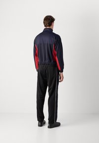 Ναυτικό και κόκκινο αθλητικό κοστούμι με υψηλό γιακά και ελαστική μέση, που περιλαμβάνει μαύρο παντελόνι με λωρίδες στο πλάι και μαύρα υποδήματα.